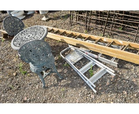 A PLASTIC ROUND GARDEN TABLE, two chairs, a parasol stand, two sets of aluminium step ladders and a wooden extension ladder