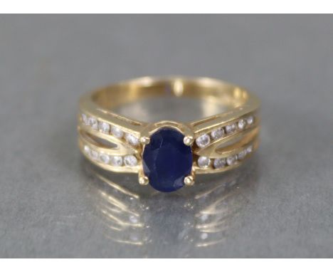 A sapphire &amp; diamond ring, the oval stone set between rows of small diamonds to the split shoulders, to a yellow metal sh