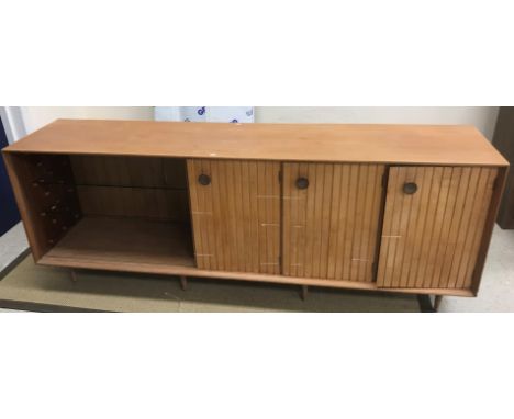 A mid 20th Century teak sideboard, the plain top above three cupboard doors with turned wooden handles enclosing glasses rack