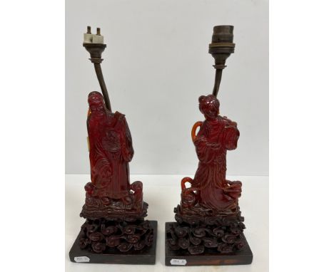 A pair of Chinese carved amber figures of a man and a woman in robes, stood upon carved wooden cloud form stands, now fitted 