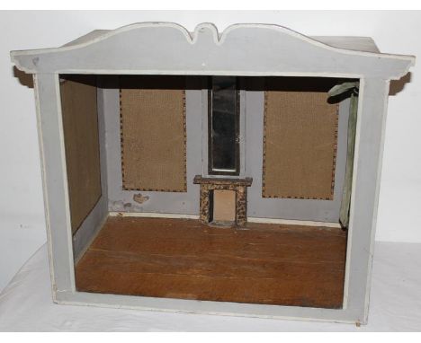 A painted wooden dolls room setting. The four outside walls are painted soft grey. The left side has a large glass window (us