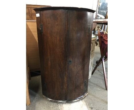 A George III oak bow-fronted hanging corner cabinet of diminutive stature  