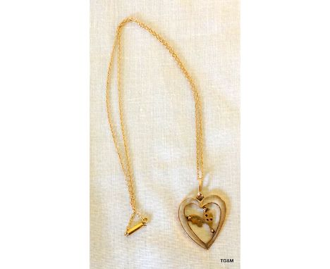 A gold heart shaped pendant set with garnet and seed pearl on gold chain