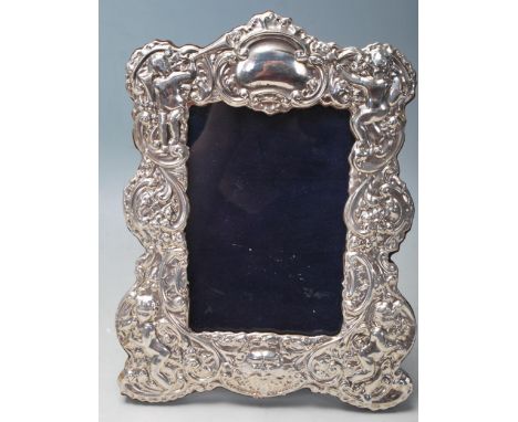 A silver and oak easel backed picture frame decorated with cherubs, puttis, a medieval greenman, foliate swirls and a central