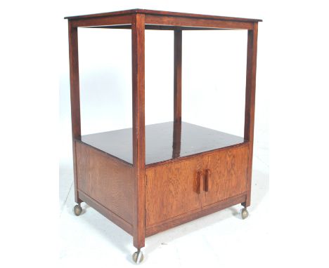 A 1930's Art deco style 2 tier drinks / cocktail trolley in oak. The trolley with a two door cupboard underneath a raised tab