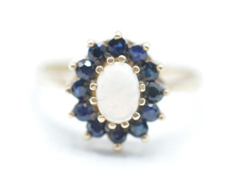 A hallmarked 9ct gold opal and blues stone ring having a central oval opal cabochon with a halo of blues stones. Hallmarked d