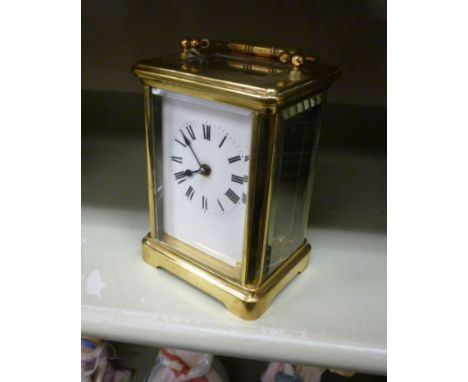 A mid 20thC lacquered brass cased carriage timepiece with a folding top handle and bevelled glass panels, on a plinth; the mo
