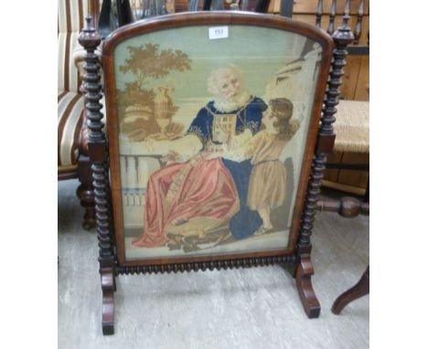 A late Victorian mahogany firescreen, set with a tapestry panel depicting a young girl and an elderly gentleman, flanked by b