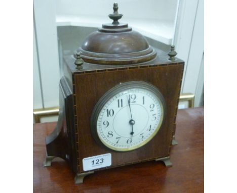 An Edwardian mahogany cased mantel timepiece with a semi-circular domed top, finials and wing flanks, on brass bracket feet; 