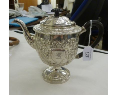 A George III silver teapot of shouldered cup design, having an ebonised handle, the hinged lid and an S-shaped spout, on a pe