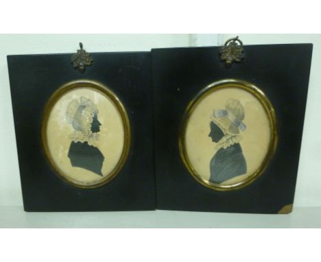 A pair of early 19thC tinted blue profile portrait silhouettes, each depicting a woman wearing a bonnet, in glazed oval frame