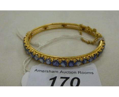 A gold coloured metal hinged bangle, set with a graduated row of circular cut sapphires, on a safety chain       11
