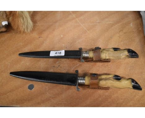 A pair of vintage hunting knives with metal scabbards and small deer hoof handles