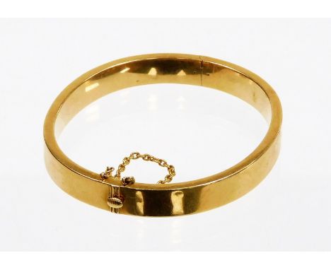 A hinged bangle, of plain design, with safety chain, yellow metal, marked 15ct to clasp, 5.5cm diameter, 14.9g all in. 