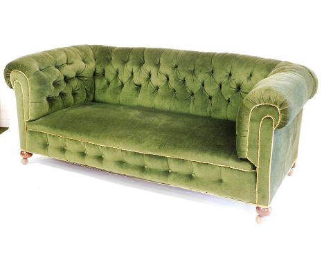 A Victorian button back Chesterfield sofa, with shaped arms, turned mahogany front bun legs terminating in castors, in later 