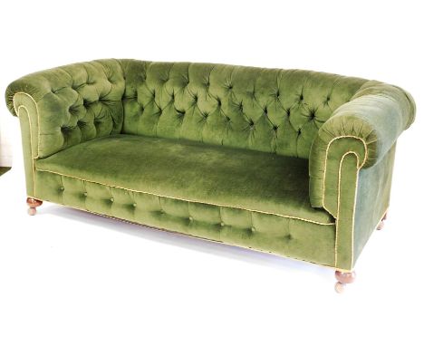 A Victorian button back Chesterfield sofa, with shaped arms, turned mahogany front bun legs terminating in castors, in later 