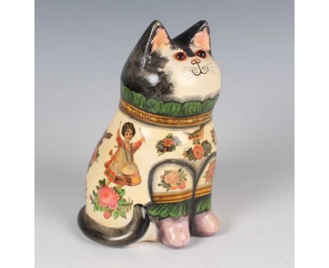 A Joan and David De Bethel Rye pottery cat, dated 1992, typically modelled seated, its cream clothing découpaged with childre