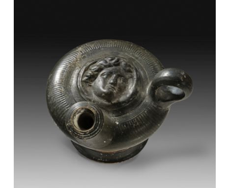Apulischer Guttus mit plastischem Dekor. 2. Hälfte 4. Jh. v. Chr. H 13,5cm, L 13,5cm, ø Körper 11cm. Glanztonware mit gerippt