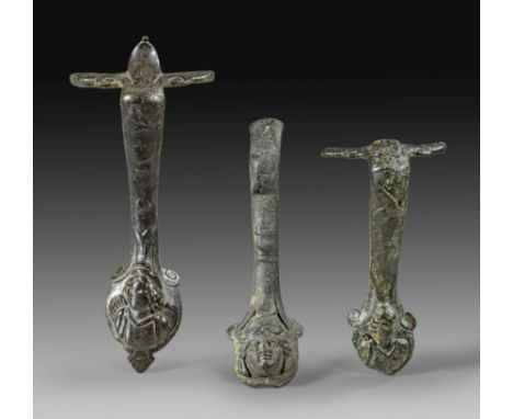 Drei bronzene Kannenhenkel. Römische Kaiserzeit, 1. - 2. Jh. n. Chr. Vollguss mit Kaltarbeit. Henkel mit Erosbüste. L 16,2cm.