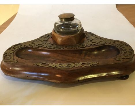 An early 20th century walnut desk stand with capstan style glass inkwell and pen well with applied brass detail plus an early