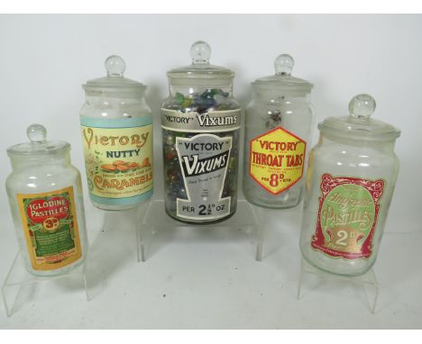 Five vintage glass sweet jars with labels, one containing marbles.