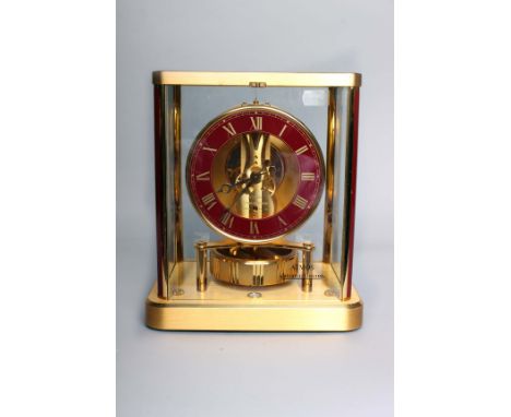 A Jaeger-Le Coultre Atmos Perpetuelle mantel clock, with a maroon dial, 23cm high, in the original cardboard packing case.