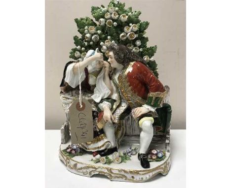 A Continental encrusted china figure group modelled as a gentleman and a lady sitting on a garden bench, height 27 cm. 