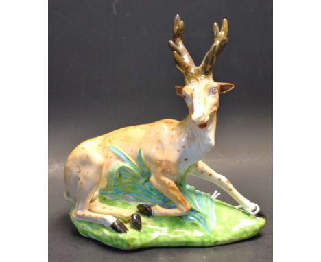A Derby model, recumbent stag, spotted in brown, green shaped oval base, 16cm high, crown, crossed batons and D mark in red, 
