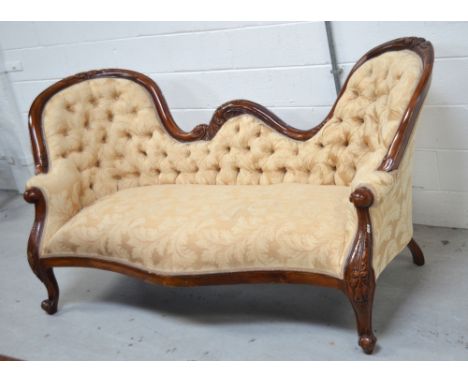 A late 19th/early 20th century walnut-framed couple's sofa, more recently upholstered with buttoned back, with carved top rai