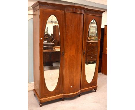 An Edwardian mahogany inlaid triple-door wardrobe with central bow-front panel and two mirrored doors to either side on turne