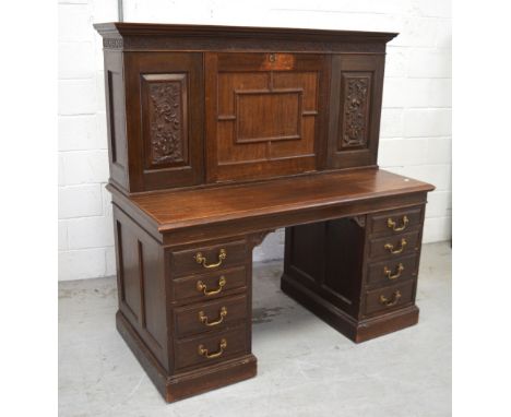 A large early 20th century oak kneehole bureau, one central drop-down door with carved panel to either side over four drawers