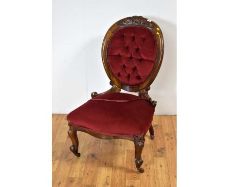 A Victorian carved walnut button-back easy chair, upholstered in plush red fabric, the top rail with carved foliate decoratio