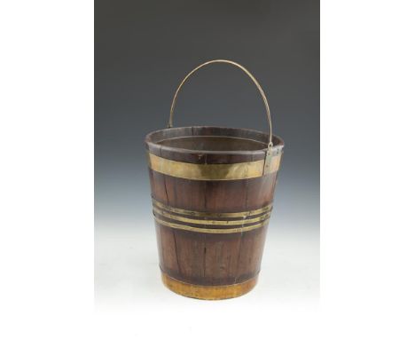 A 19TH CENTURY MAHOGANY COOPERED FUEL BUCKET of compact proportions with slender brass swing handle and brass banding, fitted
