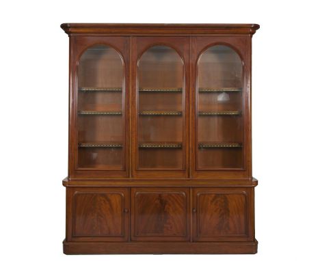 A VICTORIAN MAHOGANY BOOKCASE, the moulded cornice above three arched glazed panel doors enclosing shelves and raised on a co