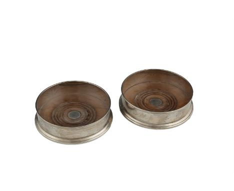 A PAIR OF MODERN SILVER CIRCULAR DECANTER COASTERS, London marks, with turned timber bases and reeded rims. 14cm diameter (2)