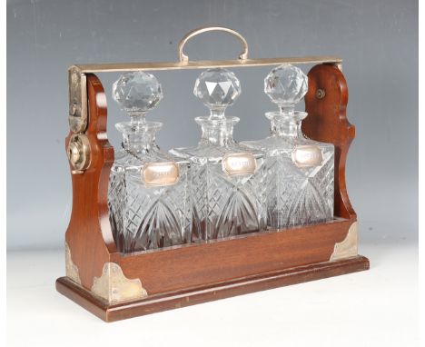 A late 20th century mahogany three-bottle tantalus, the silver plated mounts stamped 'PB &amp; S', the three glass decanters 