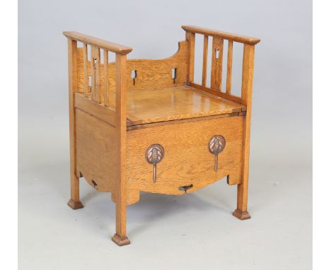 An Edwardian Arts and Crafts oak bedroom chair commode, the back supports pierced with tulips above a hinged seat, the front 