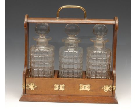 A late Victorian oak three-bottle tantalus, the fall-front base applied with brass cut-card work, 35cm wide, c.1890 