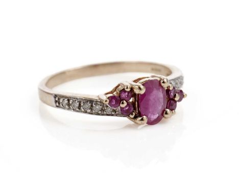 A ruby and diamond dress ring, the faceted oval ruby flanked by trios of round cut rubies, on diamond shoulders, in 9ct yello
