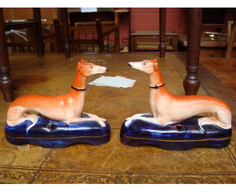 A pair of possible 19th Century Staffordshire greyhound inkwell figures, each of recumbent form, in orange and blue with gilt