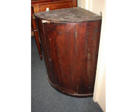 An early 19th century mahogany bow front hanging corner wall cupboard with single door enclosing shelf and red painted interi