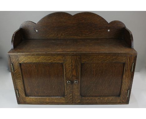 A 20th century oak wall cupboard, with raised scalloped back and two panel doors enclosing five shelves, 61cm wide