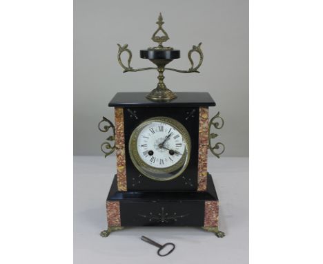 A Victorian black slate mantel clock with marble inlay, ormolu finial and paw feet, the decorative circular dial with Roman n