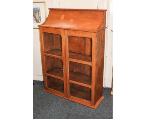 A pine wall cupboard with sloping top, twin glazed panel doors (one glass panel missing) enclosing two shelves, plinth base, 