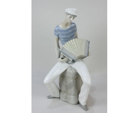 A Lladro Figure of an Accordion Player seated on a bale, designed by Salvador Furio (1970-1981), 34cm high.