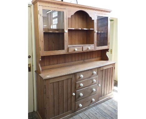 A large pine dresser with shelf back glazed cupboards and drawers over four central drawers flanked by two cupboards