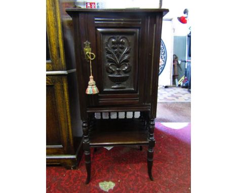 An Edwardian mahogany lamp or side cupboard enclosed by a single carved and panelled door over an open shelf, raised on turne