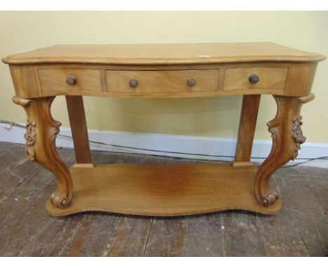 A Victorian pale mahogany side table of serpentine form, fitted with three frieze drawers, raised on carved and scrolled fore