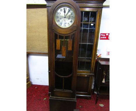 An Art Deco longcase clock, the oak cigar shaped case enclosing an anodised dial and three train movement enclosed by a parti