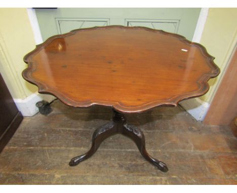 A Georgian mahogany occasional table with pie crust border raised on a turned and carved column, the tripod base with further